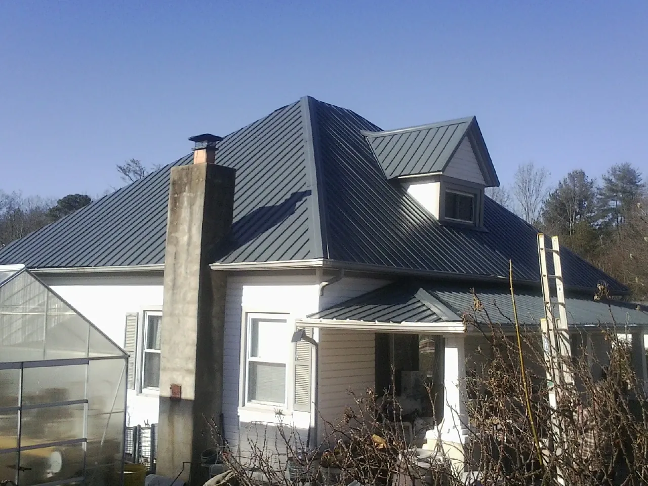 Dark blue standing seam metal roof on a white farmhouse with dormer — Slate & Tile Roof Repair by Roofing Brothers in Blodgett Mills