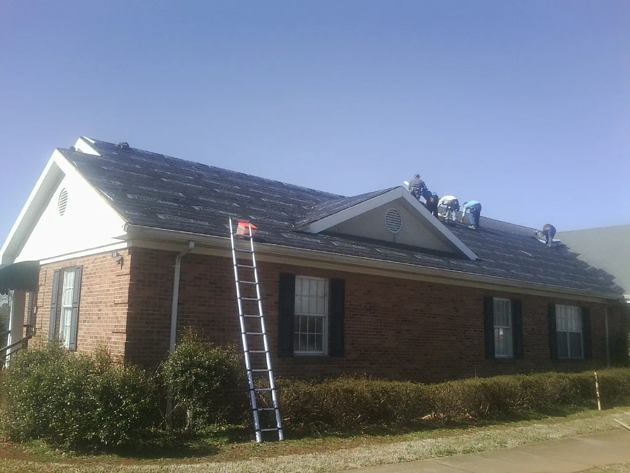 Crew tearing shingles off a brick ranch roof with a ladder set — Metal Roof Repair work by our crew in Blodgett Mills