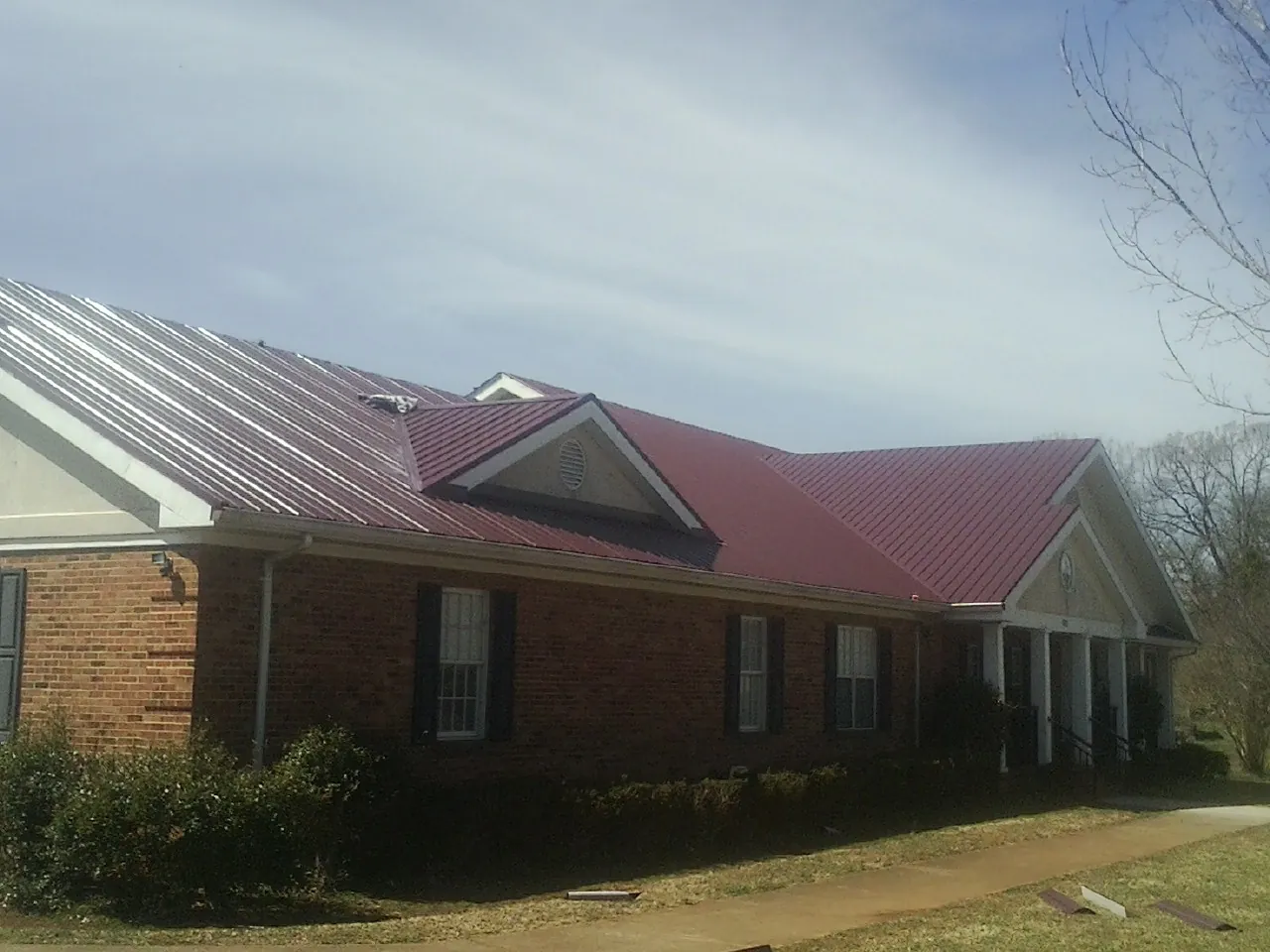 Red metal roof with gabled entries on a long brick building, from a Hail Damage Roof Repair job in Blodgett Mills