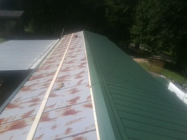 Old rusted panels beside newly installed green metal roofing — Wind Damage Roof Repair by Roofing Brothers in Blodgett Mills