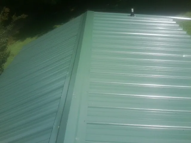 New green metal panels meeting at the ridge of a roof in Blodgett Mills