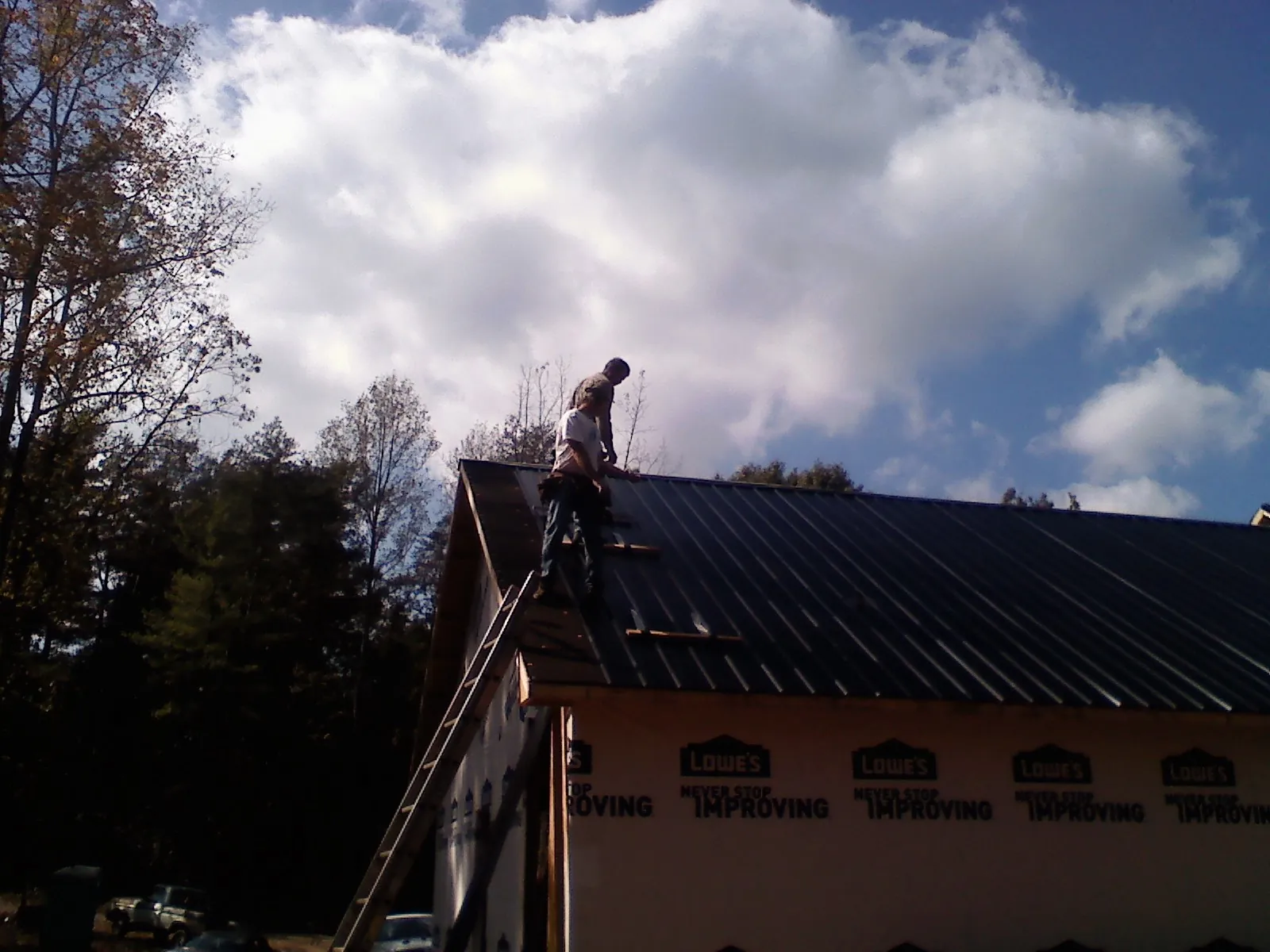 Roofer fastening dark metal panels high against a cloudy sky, from a Roof Inspection job in Blodgett Mills