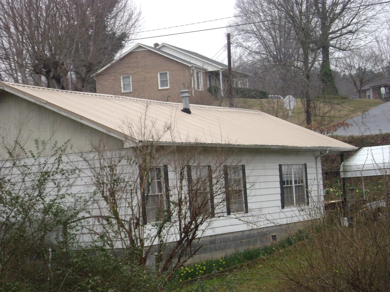 Tan metal roof on a white sided house set into a hillside — Commercial Roofing by Roofing Brothers in Blodgett Mills